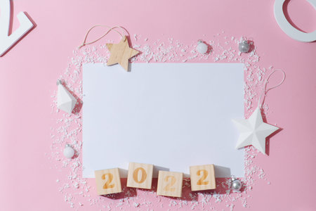Clear sheet of paper and 2022 number on cubes surrounded by new year decoration. Artificial plastic...