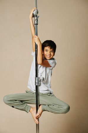 Lighthearted indian boy hanging on a pole, catching with his hands and soles. Over beige background....