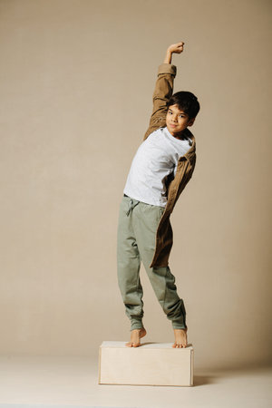 Stretching on a platform indian boy in beige oversize long sleeve shirt. Over beige background.の写真素材