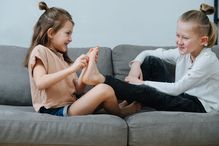 Mischievous girl trying to tickle boy's foot, they both laugh. On the couch side view.