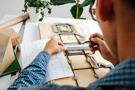 Keen box designer working on a blueprint, taking measures with a ruler. Sitting behind the desk.