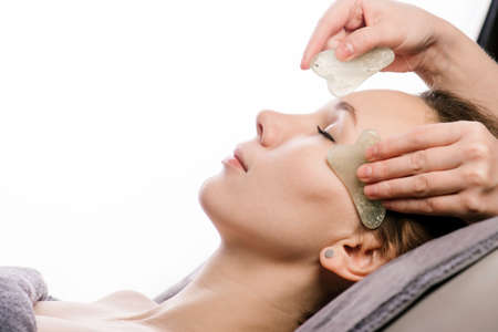 Gua sha massage of a woman in a beauty salon over white background.の写真素材