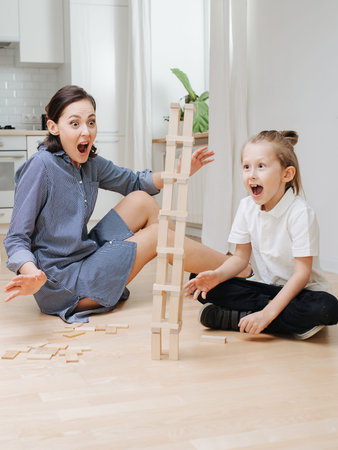 Surprised mom and son watching tower fall to side. playing on the floor.