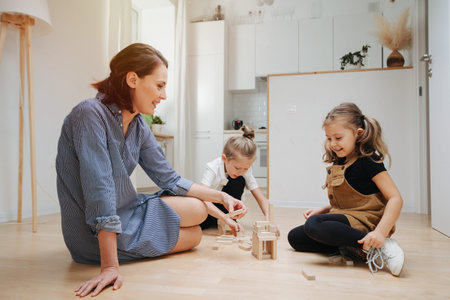 Smiling mom playing with her children on the floor. Building from wooden blocks