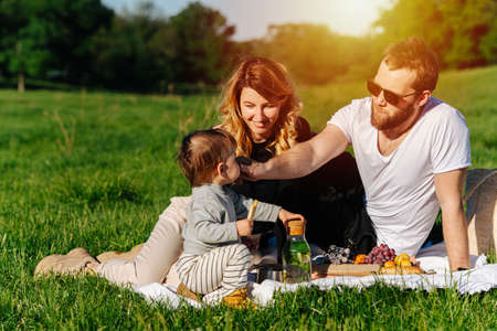 Loving young family having a picnic on a spring grassfield in a countryside. Close to trees, sun shines from above them.の写真素材