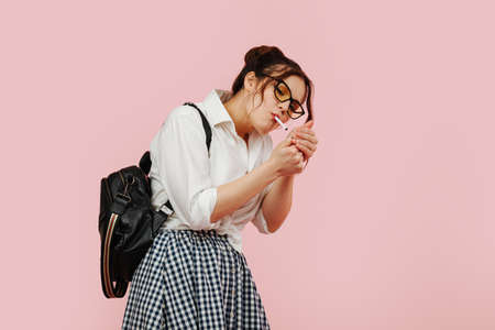 Naughty eccentric student lady lighting a smoke. Over pink background.の写真素材