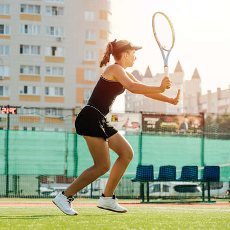 Side view of a teenage girl returning the ball, playing tennis on an outdoor tennis court. On a sunny summer evening.の写真素材
