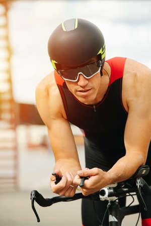 Manly muscular cyclist on his racing bike wearing helmet and sunglasses. Close shot, portrait, lit by evening sun.の写真素材