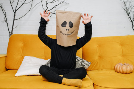 Spooky kid wearing a paper bag over his head, a scary face is drawn on it. Making claw hands....