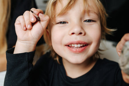 Portrait of a cute fair-headed little boy with a brush in his hand. close up.