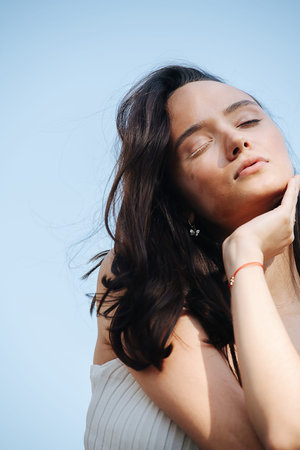 Serene brunette with vitiligo face sitting with eyes closed. Over blue sky