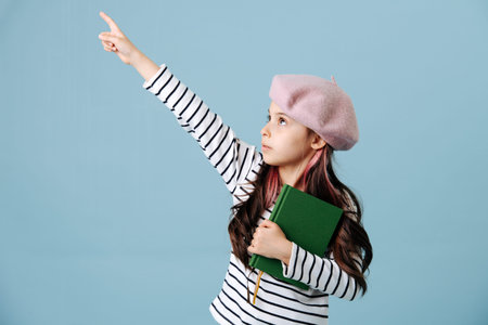 Pointing with her finger tween girl in french beret posing over blue background. She has dyed hair...