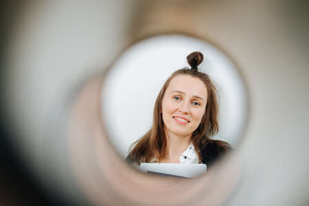 Portrait of a smiling 30 year old woman shot through a paper roll. Looking at the camera, her hair in the knot.の写真素材
