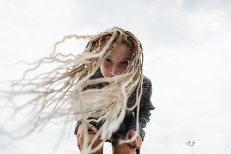 Bending forward freckled teenage girl with dreads against a gray sky. upward angle. Fluttering...