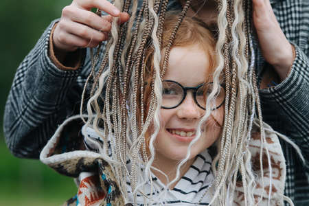 Female hands putting dreads over cute cute girl's. She is smiling, looking at the camera. Wearing glasses.の写真素材
