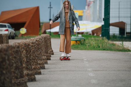 Focused girl riding on her skateboard on asphalt, having fun. next to a line of concrete car barrier