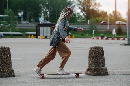 Side view of a girl riding on her skateboard on asphalt at sunset. next to a line of concrete car barrierの写真素材