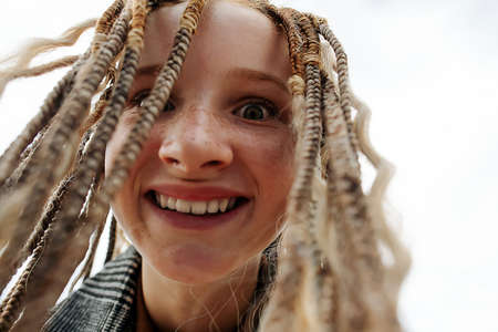 Creepy happy close up face of a freckled teenage girl with dreads. upward angle. Against a gray sky.の写真素材