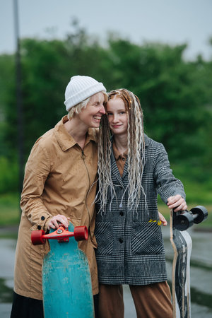 Hugging mother and daughter leaning on skateboards on a rainy day. green vegetation background.の写真素材