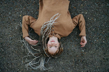 Overhead portrait of a teenager girl with dreads lying on the street asphalt. looking up at the camera.の写真素材
