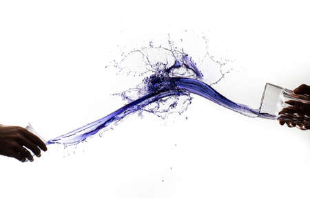 To masses of water launched from glasses splashing against each other. A contact whirlpool creating a thin film of water. Light is shining through a deep blue water mass.の写真素材