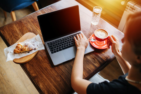 Young woman, drinking coffee and working on her laptop in a cafe.