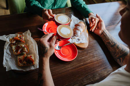 No face image of couple sitting in a cafe opposite to each other, holding handsの写真素材