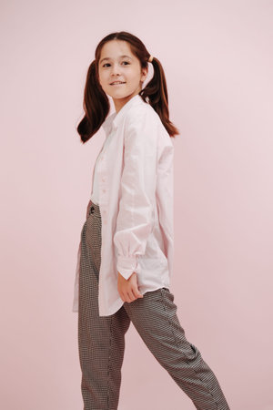 Smiling cute twelve year old girl with pigtails, stepping with her head half turned. She is wearing white shirts, black and white patterned pants over pink background.の写真素材