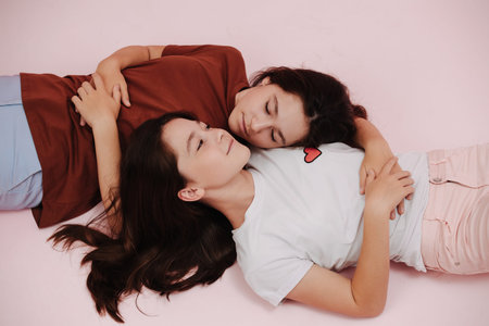 Reaxing twin girls lying on the floor in opposite directions, resting heads on one another. over...
