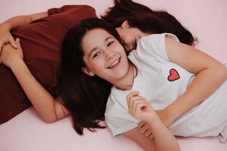 Fun twin girls dressed in different colors lying on the floor, smiling. over pink background.の写真素材