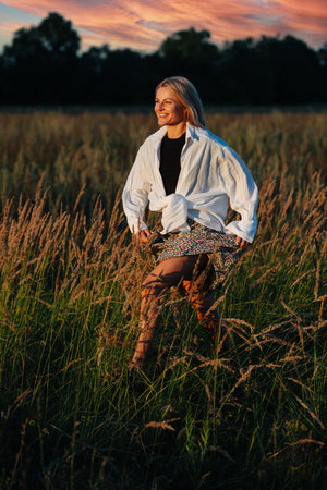 Smiling young blond woman looking straight, running through a wheat field. Holding her skirt. Blurred background.の写真素材
