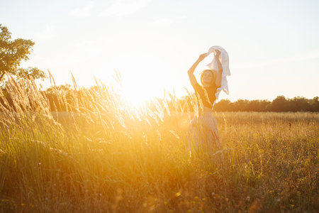 Happy young blond woman standing amidst wheat field. Against setting sunの写真素材