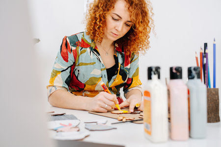 Low angle image of a woman sitting behind desk, painting wooden shapes.の写真素材