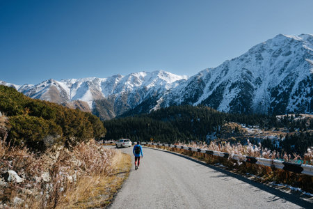 Longshot of a man walking on the road surrounded by beautiful mountain scenery. Trees by his sides...