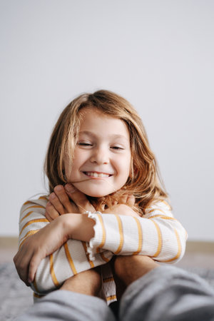 Loving blissful girl hugging her dad's feet. Smiling, eyes half closed. Blank wall behind.の写真素材