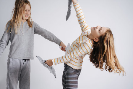 Siblings playing with paper swords, girl is pulling an act, pretending to be stubbed through. Wearing nightwear. In a room with a blank wall.の写真素材