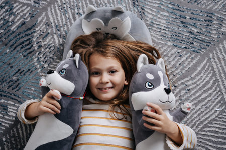 Adorable girl lying on the floor surrounded by plush huskies. Smiling at the camera.の写真素材
