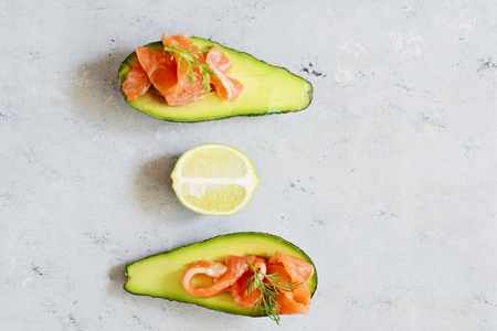 Slices of salted trout on a gray background. Avocado boats stuffed with spinach leaves and arugula, concept of healthy food, diet.の写真素材