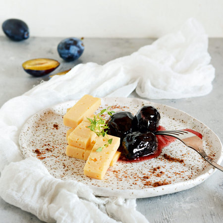 Dessert Cheese Plate with Chocolate Chips and Plum Confiture and fresh thyme. Sliced cheese on a white plateの写真素材
