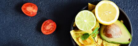 Bowl of guacamole dip with corn nachos (chips) and ingredients on a black background, selective focus. Mexican national dish.の写真素材