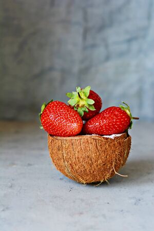 Ripe fresh strawberries in a half of coconut on a blue (gray) background. Superfood, healthy breakfast and delicious raw dessert. Healthy food concept, vegan food.の写真素材