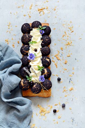 Dessert Saint Onore. Berry pie. Puff pastry tart with profiteroles, butter cream, black currant jam with fresh mint, lavender flowers and berries. Gourmet french dessert on gray background.の写真素材