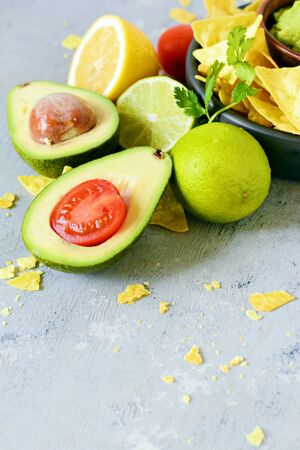 Bowl of guacamole dip with corn nachos (chips) and ingredients on a blue background, selective focus. Mexican national dish.の写真素材