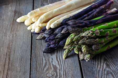 Raw white, purple, green asparagus on a dark wooden background. Raw food concept, place for copy space.の写真素材