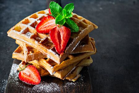 Fresh crisp Belgian waffles with ripe strawberries, mint and honey for breakfast on a wooden board on a dark background.の写真素材