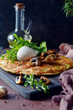 Frittata with potatoes, mushrooms, arugula and herbs for breakfast on a dark background.の写真素材