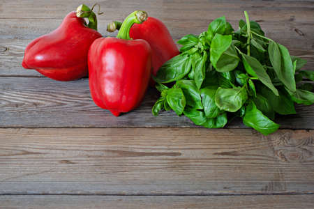 Ripe red bell pepper (paprika) with fresh green basil on wooden background, healthy food concept, vegan food.の写真素材