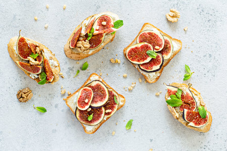 Crispy bruschetta with soft ricotta, ripe figs, walnuts and pine nuts, mint and honey on a light...