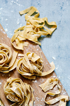 Raw yellow homemade italian pasta pappardelle, fettuccine or tagliatelle on a blue background, close up. Egg homemade noodles cooking process, long rolled macaroni, uncooked spaghetti.の写真素材