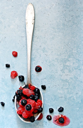 Frozen (thawed) cherries, blueberries, red currants in a spoon on a blue background. Healthy fruits,...